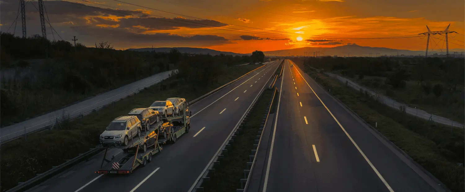 A car carrier truck is transporting several cars during sunset