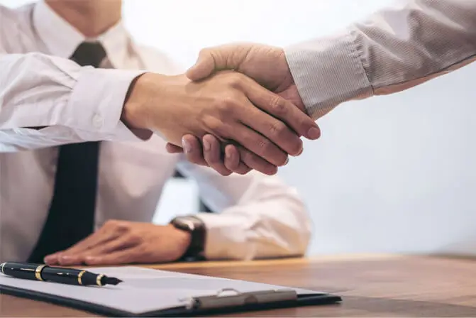 Two people wearing long-sleeved polo shirts shake hands.