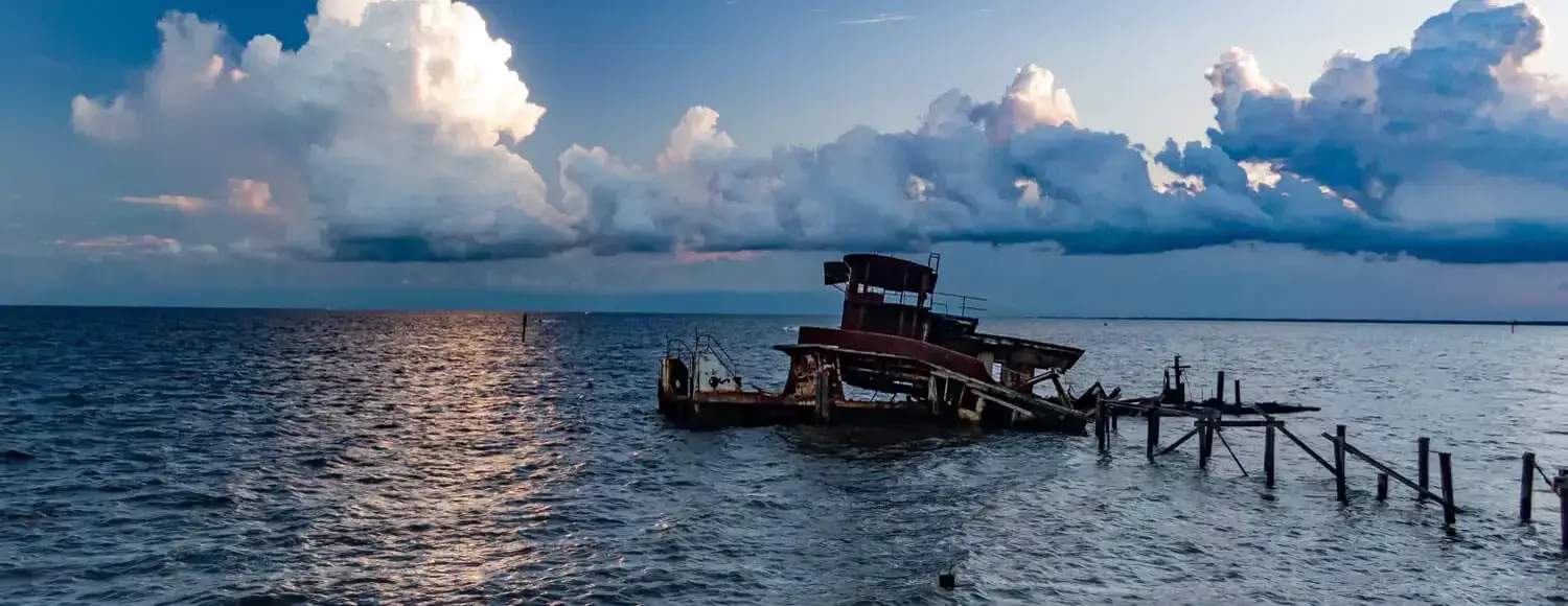 The remains of a wooden shipwreck lie submerged in the ocean, with its broken mast jutting out of the water.